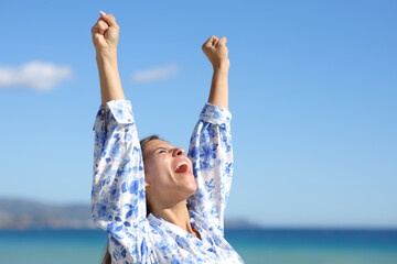 Excited woman raising arms on the beach celebrating