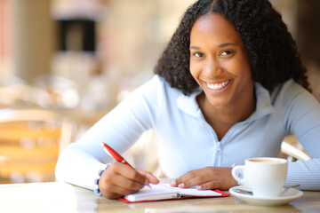 Happy black woman looks at you writing in agenda