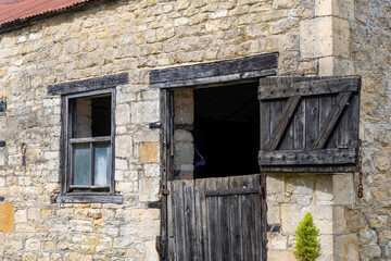 Close up view of weathered black wooden door and window of a stable in the Cotswolds, UK with typical walls of limestone or Cotswold stone