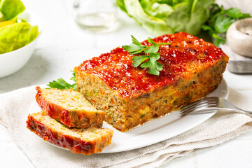 Meatloaf or terrine with chicken and turkey meat, carrot,  leek and green peas, glazed with ketchup. Baked minced chicken meat. White table surface.