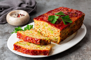 Homemade meatloaf or terrine with mix of chicken and turkey meat, carrot, leek and green peas, glazed with ketchup. Oven Baked food. Grey background.