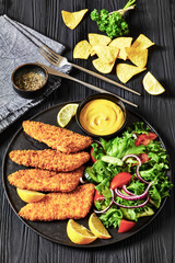 breaded fish fillet with salad on black plate