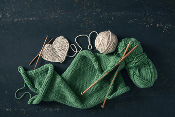 Knitting project with white and green wool and bamboo needles on rustic background.