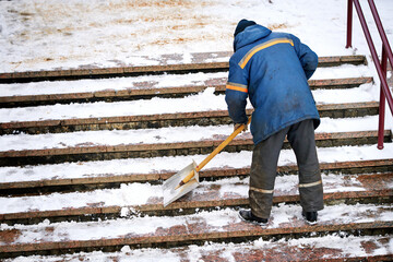 Сleaning stairs steps from snow after blizard, snow removal work. Worker with snow shovel removing...