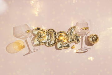 Happy New Year holiday flat lay, text 2024 golden balloon on pastel pink background, shiny wine glasses, Christmas transparent ball and mirror disco ball. Star filter effect, double exposition