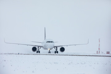Traffic at airport during snowfall. Passenger airplane taxiing to runway for take off on frosty winter day..