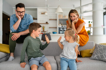 Tired parents sitting on couch feels annoyed exhausted while happy children playing together.