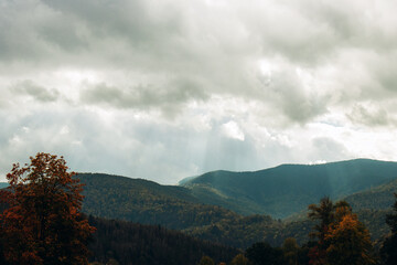 Obraz premium Image of a landscape overlooking mountain forests. The rays of the sun illuminate the forest land. Clouds covered the sky. Travel to quiet, peaceful places. Can be used as banner background, wallpaper