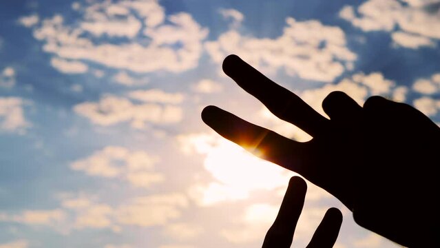 Silhouettes of four hands are showing victory sign, gesture of peace against the sunset or sunrise sky - close up, sun lens flare. Unity, harmony, friendship and positive concept