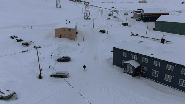 Drone view in Svalbard flying over Longyearbyen town showing a person in a black coat walking between houses in a snowy area with mountains in Norway