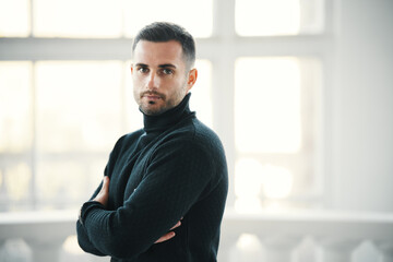Confident handsome man in a black turtleneck stands with arms crossed