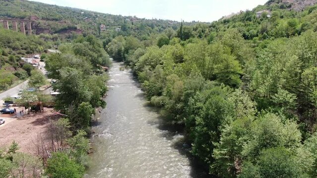Drone view in Albania vertical lift over rapids river between green mountains and a big column bridge on a sunny day