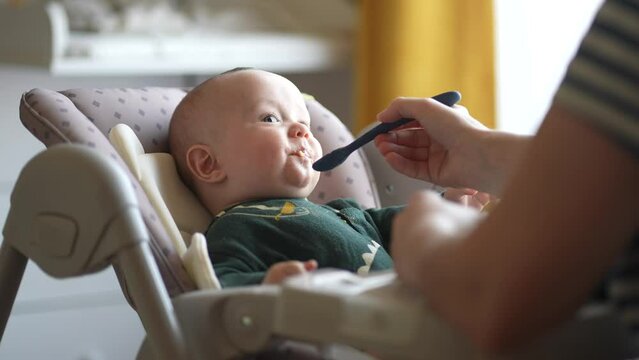 baby newborn eats. happy family dream weaning concept. dirty mess baby boy eating vegetables. baby indoors son eats on a feeding chair dirty face. naughty dirty babe indulges while feeding
