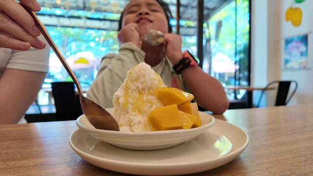 Small girl sitting indoor enjoy eating mango ice cream.