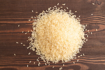 Pile of uncooked white rice on brown wooden. Top view.