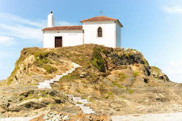 Fototapeta na wymiar White stairs leading up from the beach to a small white chapel with a bell tower on a hill.