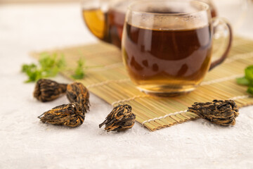 Red tea with herbs in glass on gray concrete. Side view, selective focus.