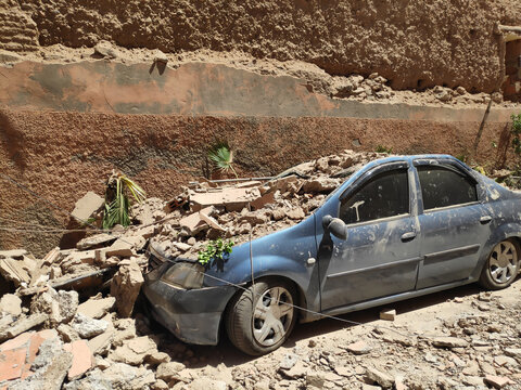 Blue car damaged, destroyed by falling rubble from collapsed wall after earthquake.