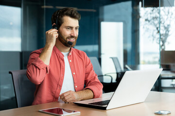 Naklejka premium Customer service representative with headset phone consults customer buyer, joyful man uses laptop for video call, businessman in shirt at workplace inside office happy and smiling.