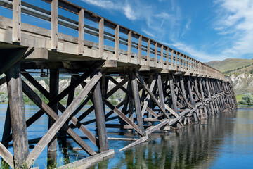 Full length view of wooden Pritchard Bridge (stringer bridge) across Thompson River, Pritchard, Canada, with in forefront blooming baby blue eyes or Nemophila menziesii and narrow bridge sign
