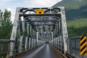 Drivers perspective of a steel truss bridge across the river in mountainous area of Canada with...