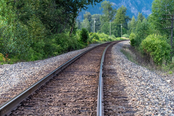 Fototapeta premium Low angle view over railroad tracks in a mountainous and forest area, curving and disappearing in the distance between the trees in Western Canada