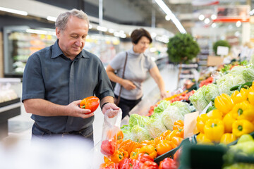 Fototapeta na wymiar Mature customer selects bell peppers with interest in grocery department of supermarket