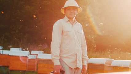 Portrait of professional beekeeper in special uniform looking at camera and smiling. Apiary, honey...