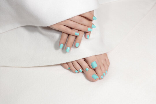 Beautiful pedicure and manicure. Close-up of pretty female toes and fingers with mint color nails. Feet and hands are covered with whte blanket. 