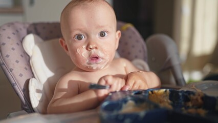baby dirty eats. happy family a child toddler concept. baby dirty lifestyle sitting messing with food at the table for feeding in the kitchen. grimy toddler in the kitchen