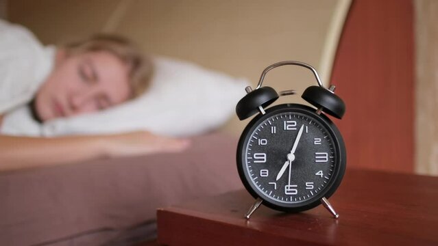 Woman waking up with alarm clock ringing at 7 o'clock, everyday morning routine.