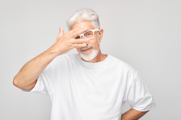 Portrait of elderly man covering eyes with hand, peeking through fingers isolated on white studio...