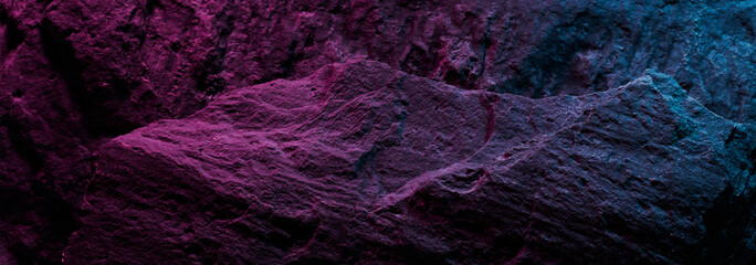 Black stone texture in pink blue neon lighting, dark abstract background. Natural mineral rock close up details, empty backdrop with copy space for design