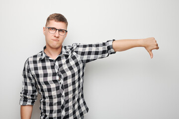 Portrait of man in shirt and glasses showing thumbs down isolated on white studio background. Dislike, wrong choice, negative evaluation concept.