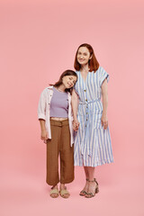 full length of cheerful woman with teen daughter holding hands and smiling at camera on pink