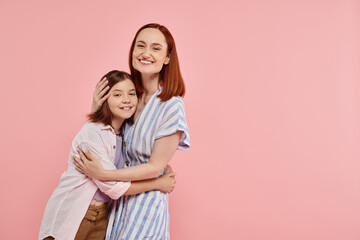 happy woman with teenage daughter in stylish casual attire looking at camera on pink backdrop