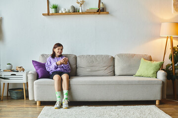 joyful teenage girl browsing social media while sitting on comfortable couch in modern living room