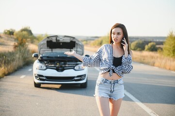 The young girl broke the car and she opened the hood and tried to repair the car on the road. A woman calls on a smartphone with a car evacuation service