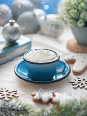 Enameled cup with whipped cream on a rustic background with beautiful Christmas lights in the form of a side. There may also be coffee. Blurred background.