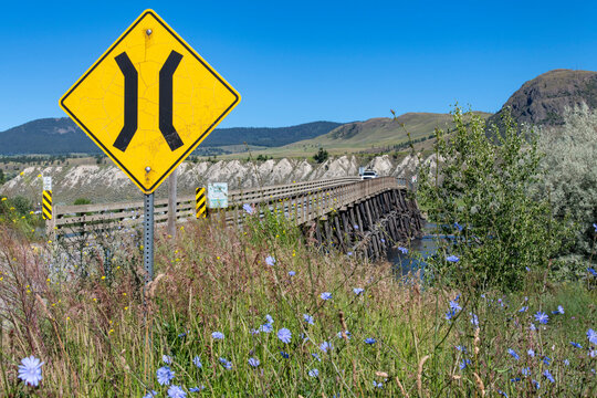 Full length view of wooden Pritchard Bridge (stringer bridge) across Thompson River, Pritchard, Canada, with in forefront blooming baby blue eyes or Nemophila menziesii and narrow bridge sign