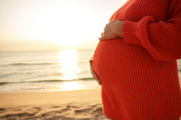 Pregnant woman with hands on stomach at beach