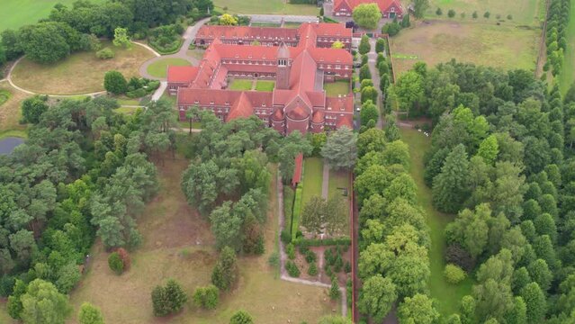 The flyover footage showcases an aerial view of the Abbey of Our Lady of Nazareth in Brecht, Belgium, nestled amidst lush greenery. The majestic red-roofed structure radiates a sense of historical