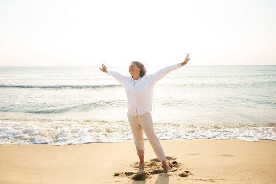 Carefree mature woman with arms outstretched standing at beach