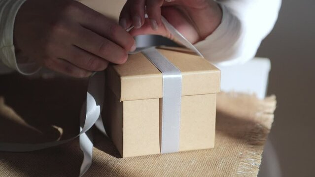 hands tying a box with a gift with a bow, holiday gift concept, preparation for birthday or Christmas celebration. close shot