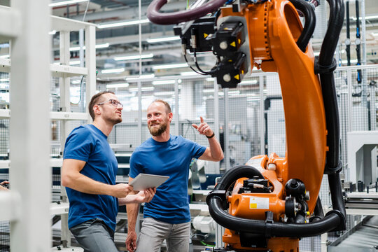 Two technicians with digital tablet examining industrial robot in a factory