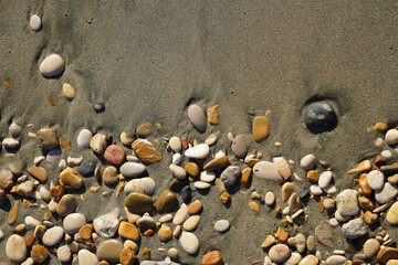 Colorful stones on a background of beach sand. The beach shore with sand and pebbles, washed by the sea waves.