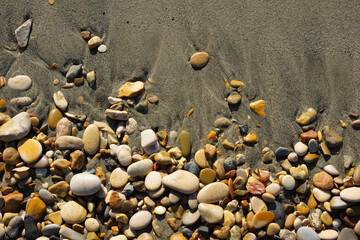 Natural colorful sea stones on a sandy beach on a sunny day, top view. Rocky sand on the beach. Marine background