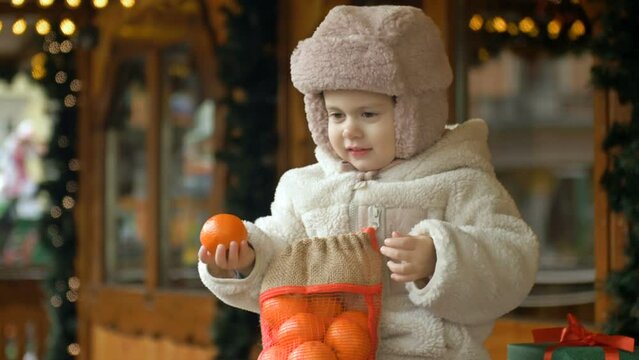 Little warmly dressed girl is holding a bag of tangerines. At the Christmas market.