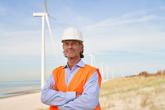 Thoughtful engineer wearing hardhat standing in front of wind turbines