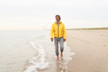 Senior man wearing yellow jacket and walking at beach